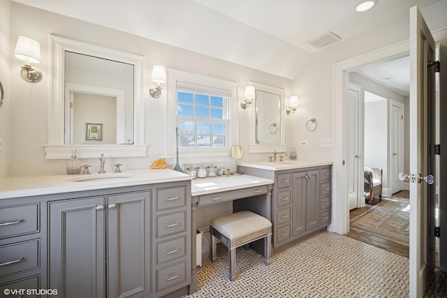 full bathroom featuring two vanities, lofted ceiling, visible vents, and a sink