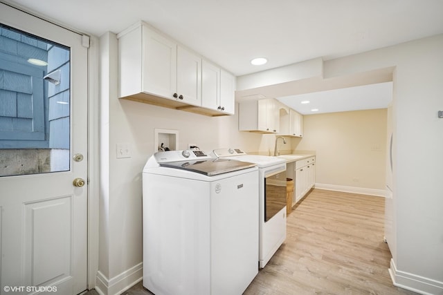 laundry room with cabinet space, baseboards, light wood-style flooring, washing machine and dryer, and a sink