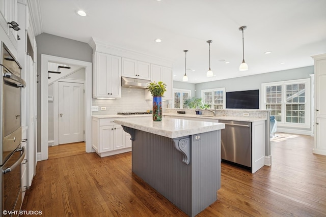 kitchen with under cabinet range hood, white cabinets, appliances with stainless steel finishes, a center island, and tasteful backsplash