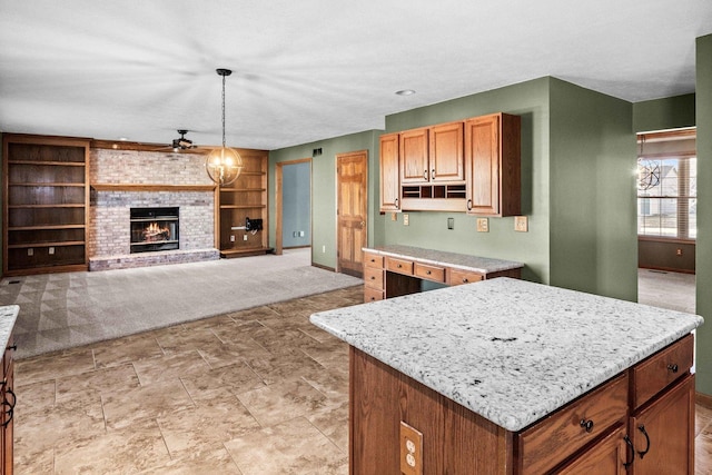 kitchen featuring built in shelves, light colored carpet, a fireplace, a ceiling fan, and pendant lighting