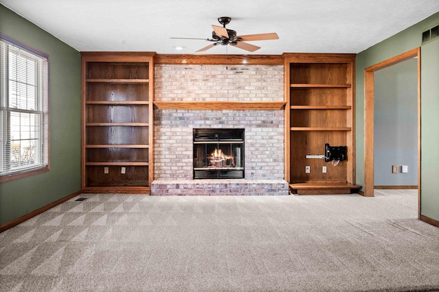 unfurnished living room with a ceiling fan, baseboards, built in features, a brick fireplace, and carpet