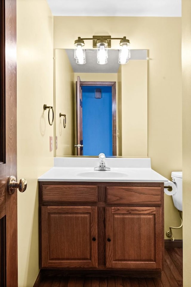 half bath featuring vanity, toilet, and wood finished floors