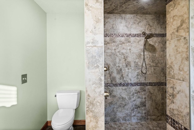 bathroom featuring baseboards, a tile shower, and toilet