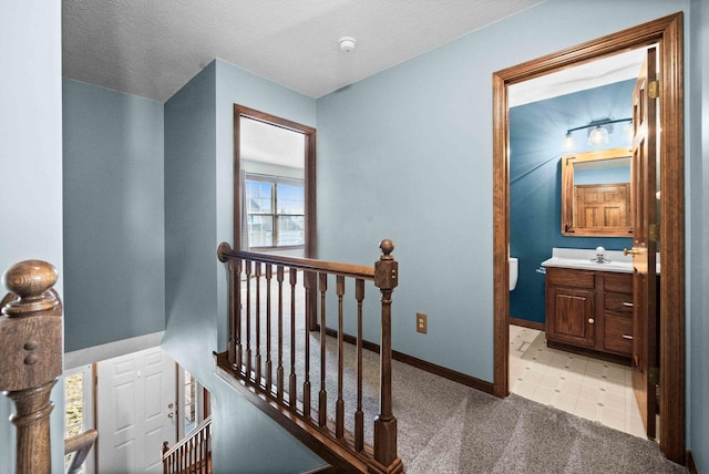 corridor featuring baseboards, light colored carpet, a sink, and an upstairs landing