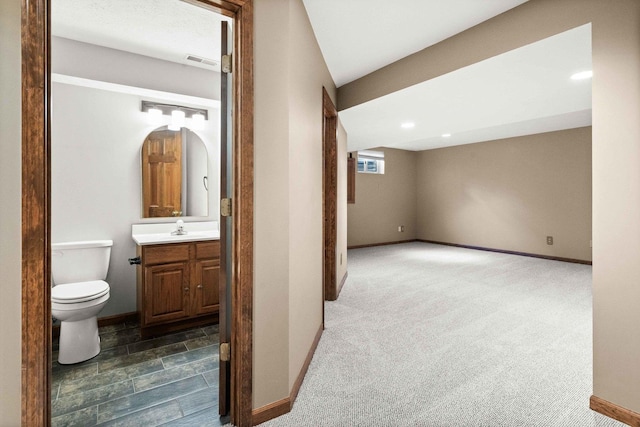 hallway with dark colored carpet, visible vents, a sink, and baseboards