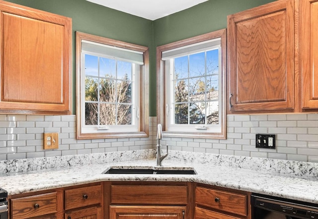 kitchen featuring black dishwasher, brown cabinets, a sink, and decorative backsplash