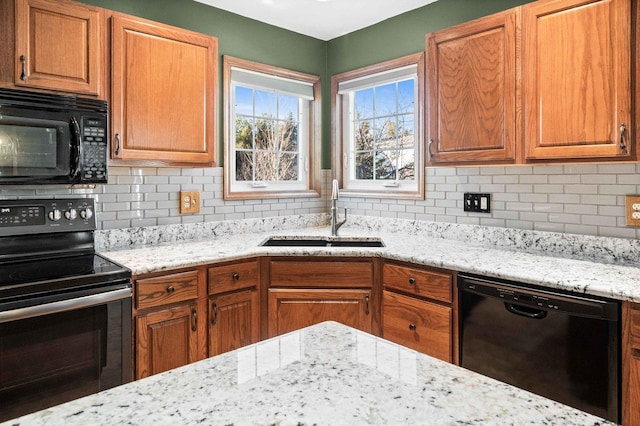 kitchen with light stone countertops, a sink, decorative backsplash, brown cabinets, and black appliances