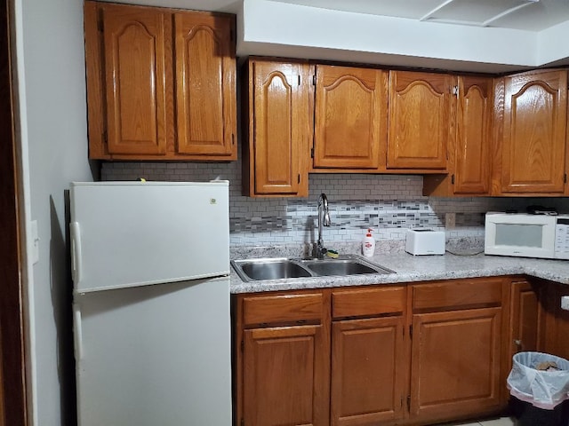 kitchen with brown cabinets, white appliances, light countertops, and a sink