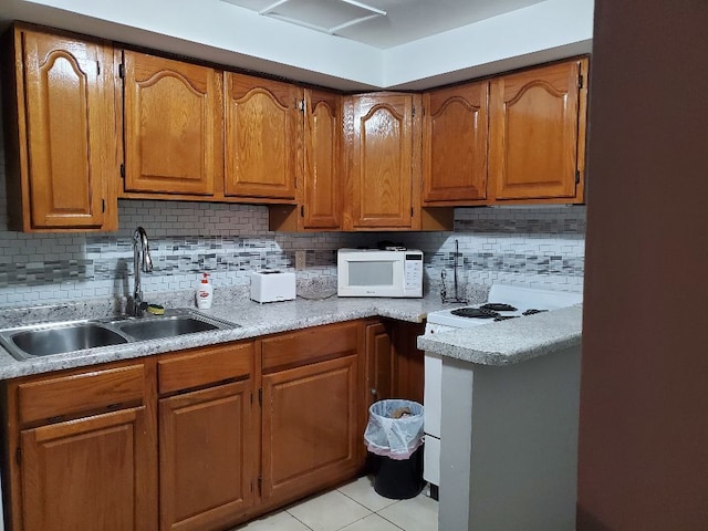 kitchen with brown cabinets, light countertops, white microwave, light tile patterned flooring, and a sink