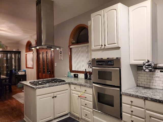 kitchen featuring stainless steel appliances, decorative backsplash, white cabinetry, island range hood, and a peninsula