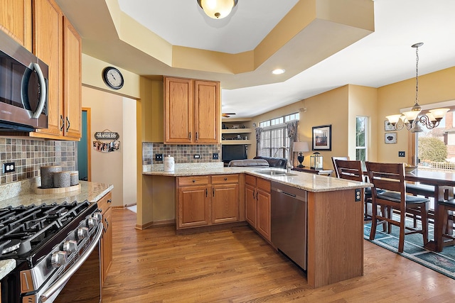 kitchen featuring a raised ceiling, a peninsula, hanging light fixtures, stainless steel appliances, and a sink