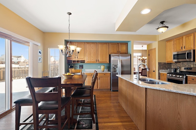 kitchen with appliances with stainless steel finishes, a sink, light stone counters, and an inviting chandelier