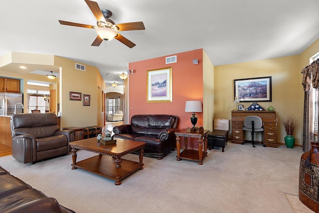 living room featuring ceiling fan, visible vents, arched walkways, and light colored carpet