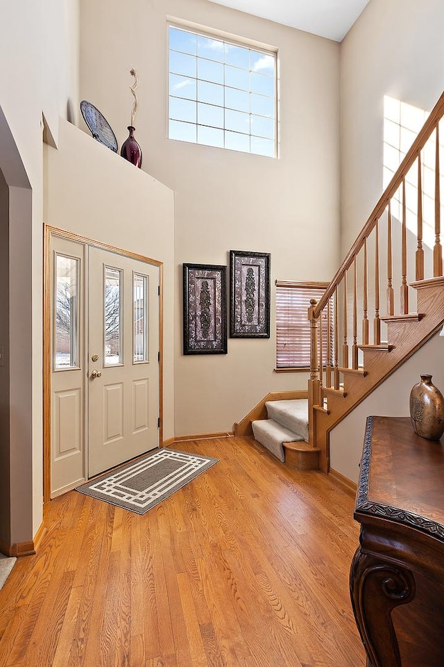 entryway featuring baseboards, a high ceiling, light wood finished floors, and stairs