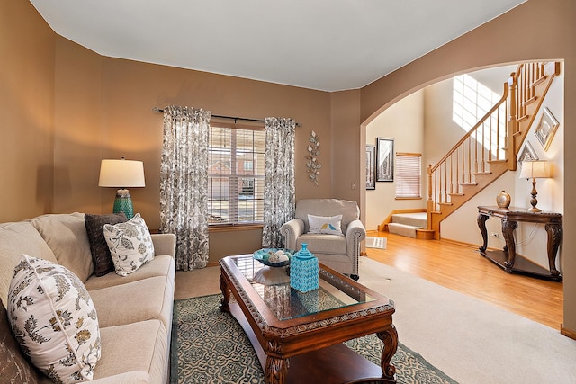 living area with baseboards, stairway, arched walkways, and wood finished floors