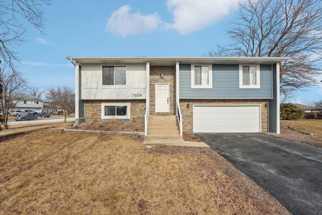 raised ranch with a garage, driveway, and stone siding