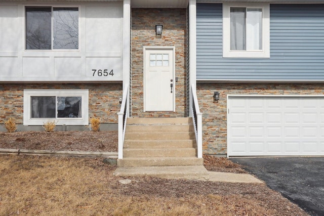 entrance to property featuring an attached garage, stone siding, and driveway