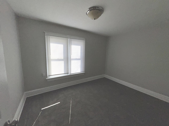 unfurnished room featuring dark carpet and baseboards