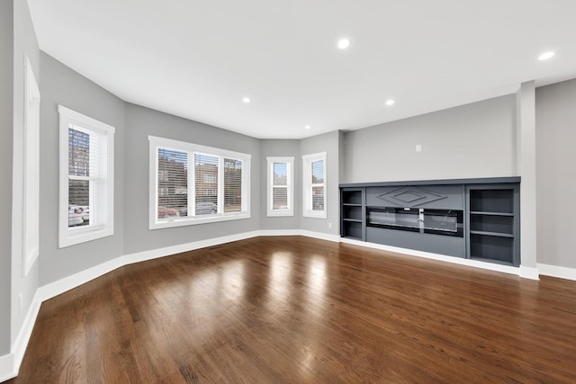 unfurnished living room with wood finished floors, recessed lighting, a glass covered fireplace, and a healthy amount of sunlight