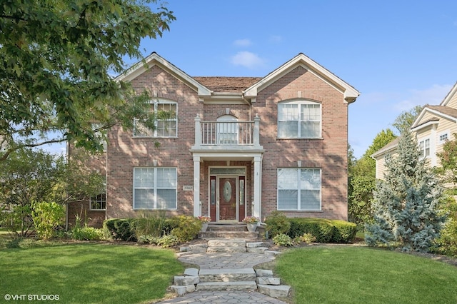 view of front of home with a balcony, a front yard, and brick siding