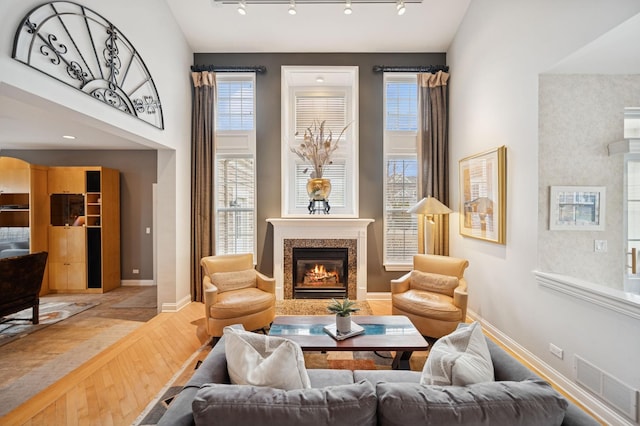 living area with baseboards, visible vents, wood finished floors, a high ceiling, and a high end fireplace