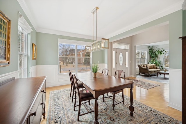 dining room with light wood-style floors, wainscoting, crown molding, and a notable chandelier