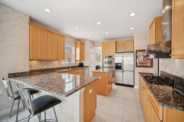 kitchen with dark stone counters, wall chimney exhaust hood, a peninsula, stainless steel appliances, and a sink