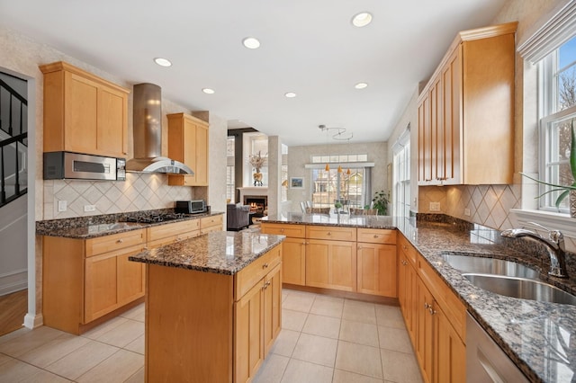 kitchen with a wealth of natural light, wall chimney range hood, a sink, and appliances with stainless steel finishes