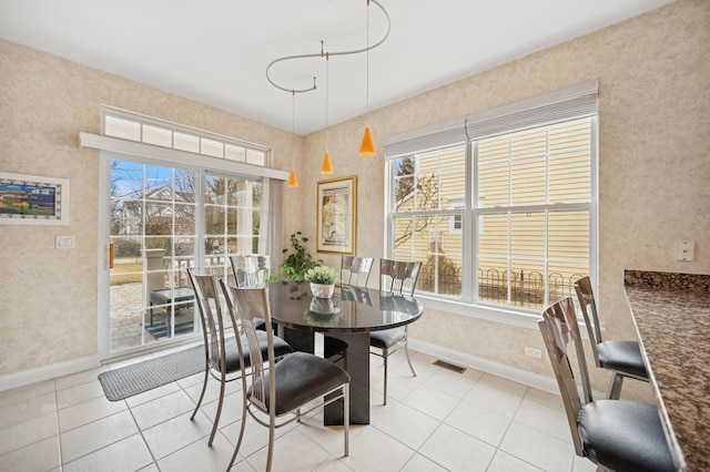 tiled dining room featuring a healthy amount of sunlight, visible vents, and baseboards