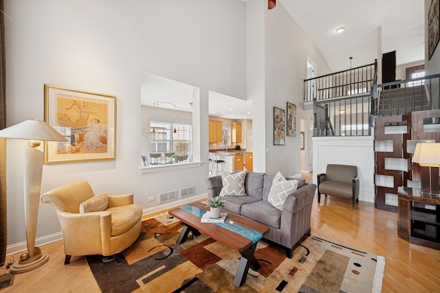 living room featuring visible vents, stairway, a high ceiling, wood finished floors, and baseboards