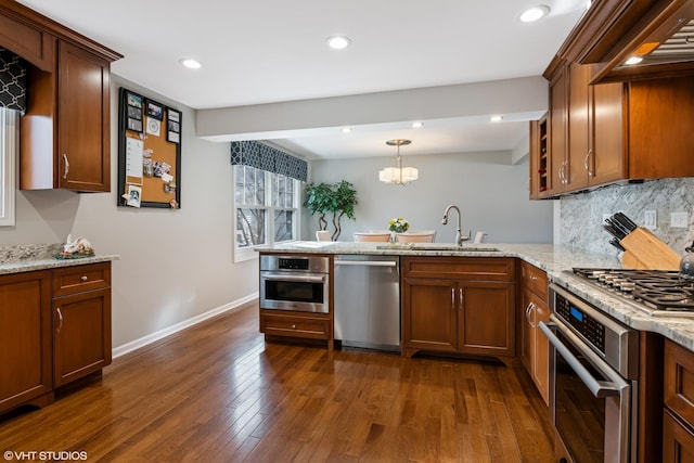 kitchen featuring dark wood finished floors, a peninsula, a sink, appliances with stainless steel finishes, and backsplash