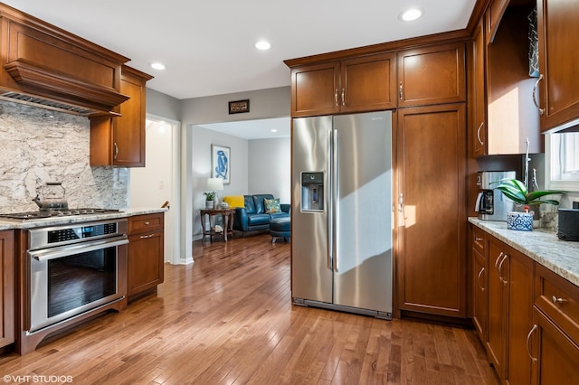 kitchen with light wood-type flooring, stainless steel appliances, light stone countertops, and custom exhaust hood