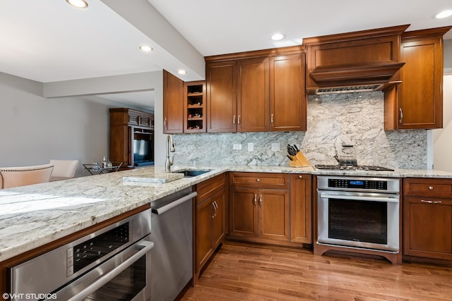 kitchen with a sink, light stone counters, light wood-style flooring, stainless steel appliances, and open shelves