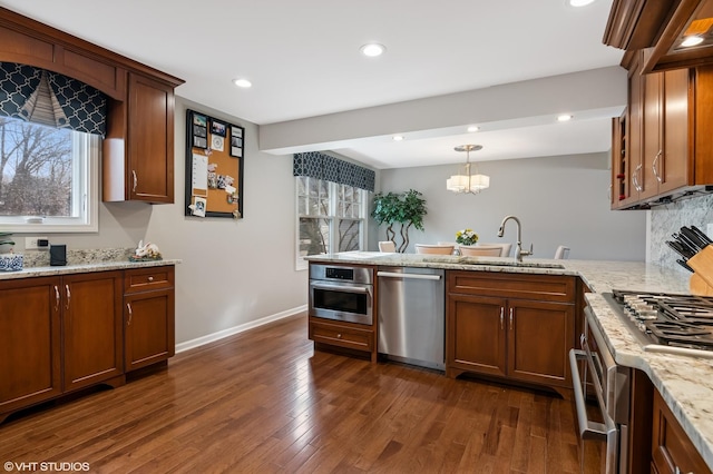 kitchen with a sink, dark wood-style floors, appliances with stainless steel finishes, a peninsula, and baseboards