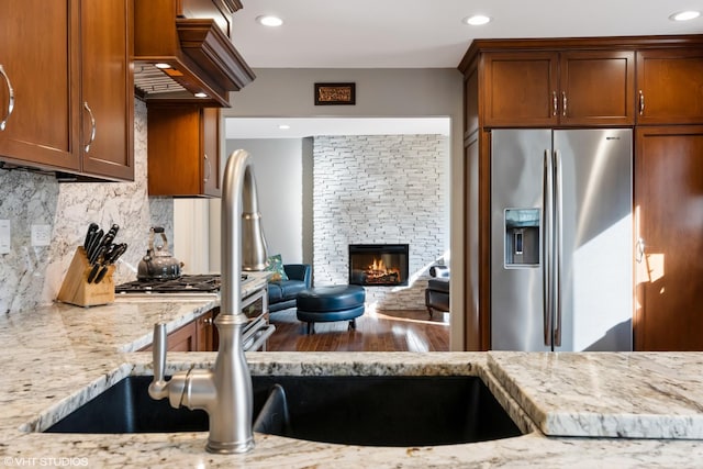 kitchen with backsplash, recessed lighting, stainless steel fridge, a fireplace, and light stone countertops