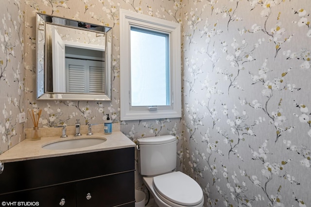 bathroom with toilet, vanity, and wallpapered walls