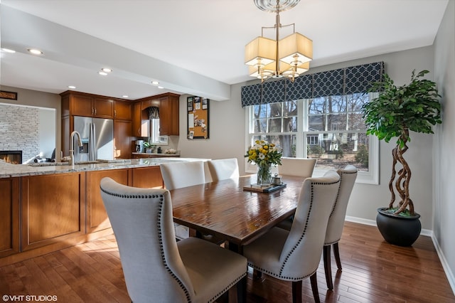 dining area with dark wood-type flooring, recessed lighting, an inviting chandelier, a stone fireplace, and baseboards