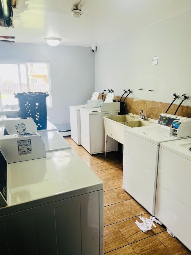 common laundry area with baseboard heating, independent washer and dryer, a sink, and light tile patterned floors