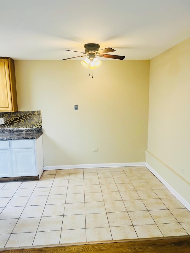 kitchen featuring light tile patterned floors, dark countertops, decorative backsplash, a ceiling fan, and baseboards