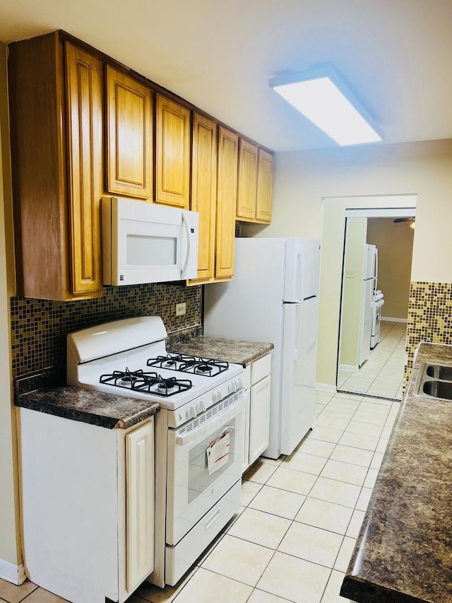 kitchen featuring light tile patterned floors, dark countertops, decorative backsplash, a sink, and white appliances