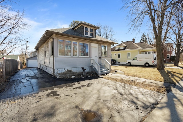 bungalow featuring a garage, roof with shingles, an outdoor structure, and fence