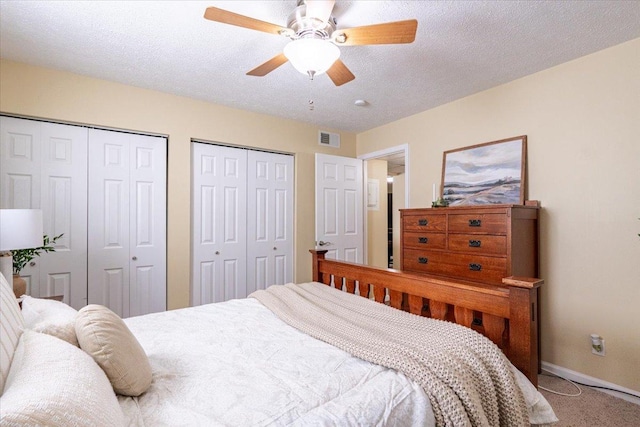 bedroom featuring a textured ceiling, carpet flooring, visible vents, baseboards, and multiple closets