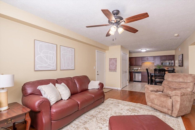 living area featuring a ceiling fan, baseboards, a textured ceiling, and light wood finished floors