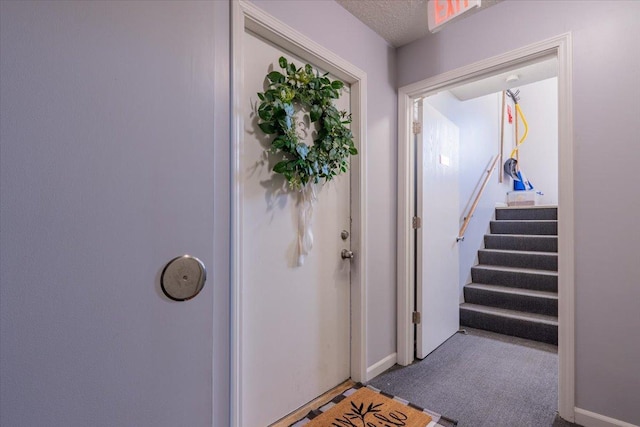 interior space featuring dark colored carpet, a textured ceiling, baseboards, and stairs