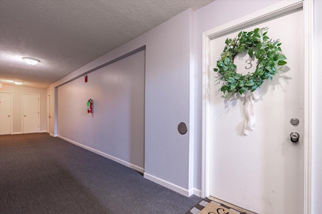 hallway featuring baseboards, dark carpet, and a textured ceiling