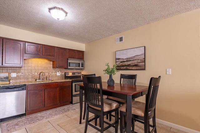 kitchen with stainless steel appliances, tasteful backsplash, visible vents, a sink, and dark brown cabinets