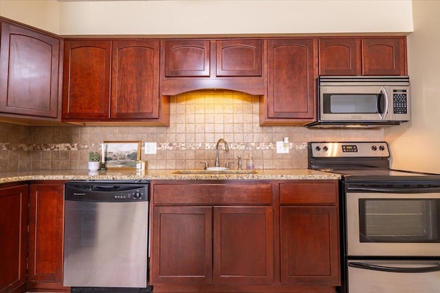 kitchen with light stone countertops, appliances with stainless steel finishes, decorative backsplash, and a sink