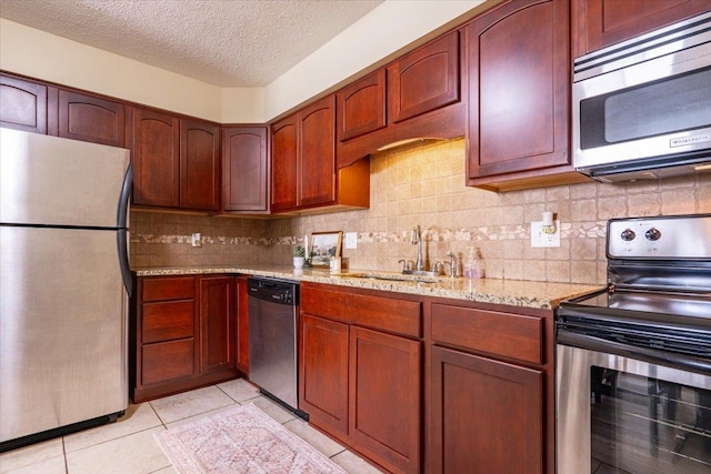 kitchen with light tile patterned flooring, stainless steel appliances, a sink, backsplash, and light stone countertops