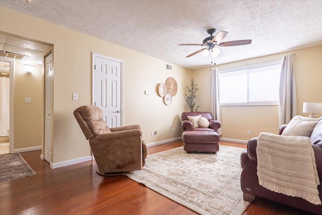 living room with ceiling fan, a textured ceiling, baseboards, and dark wood-style flooring