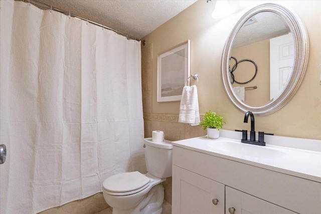 bathroom with a wainscoted wall, tile walls, toilet, a textured ceiling, and vanity